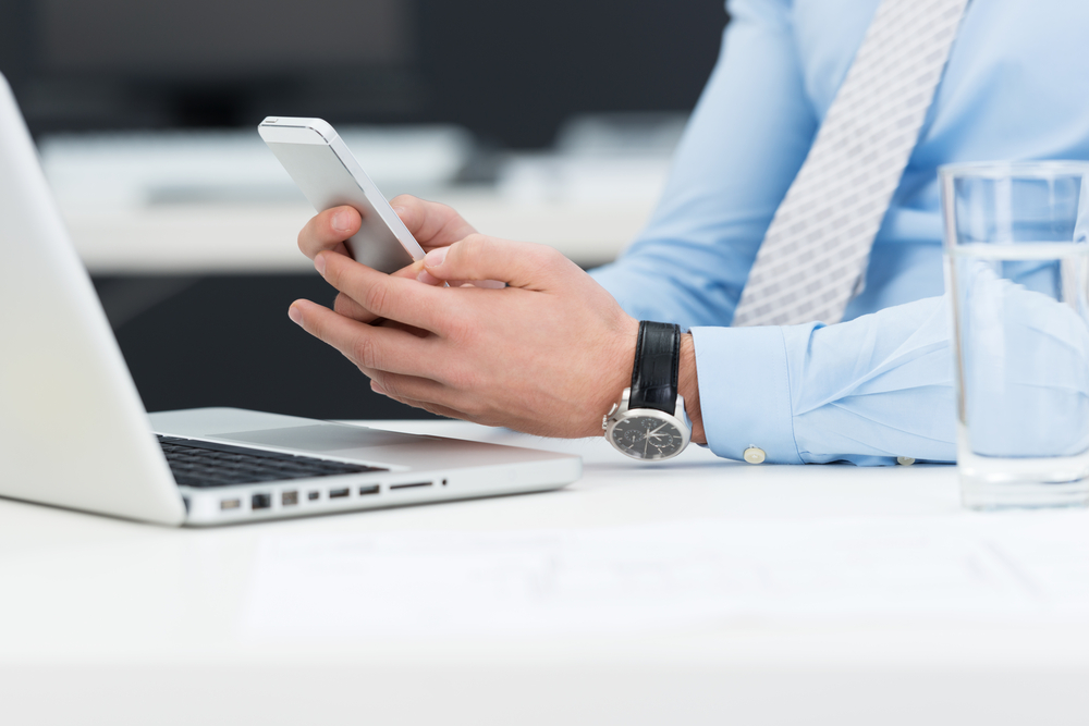 Businessman reading an sms on his mobile phone as he sits at his desk, close up view of his hands